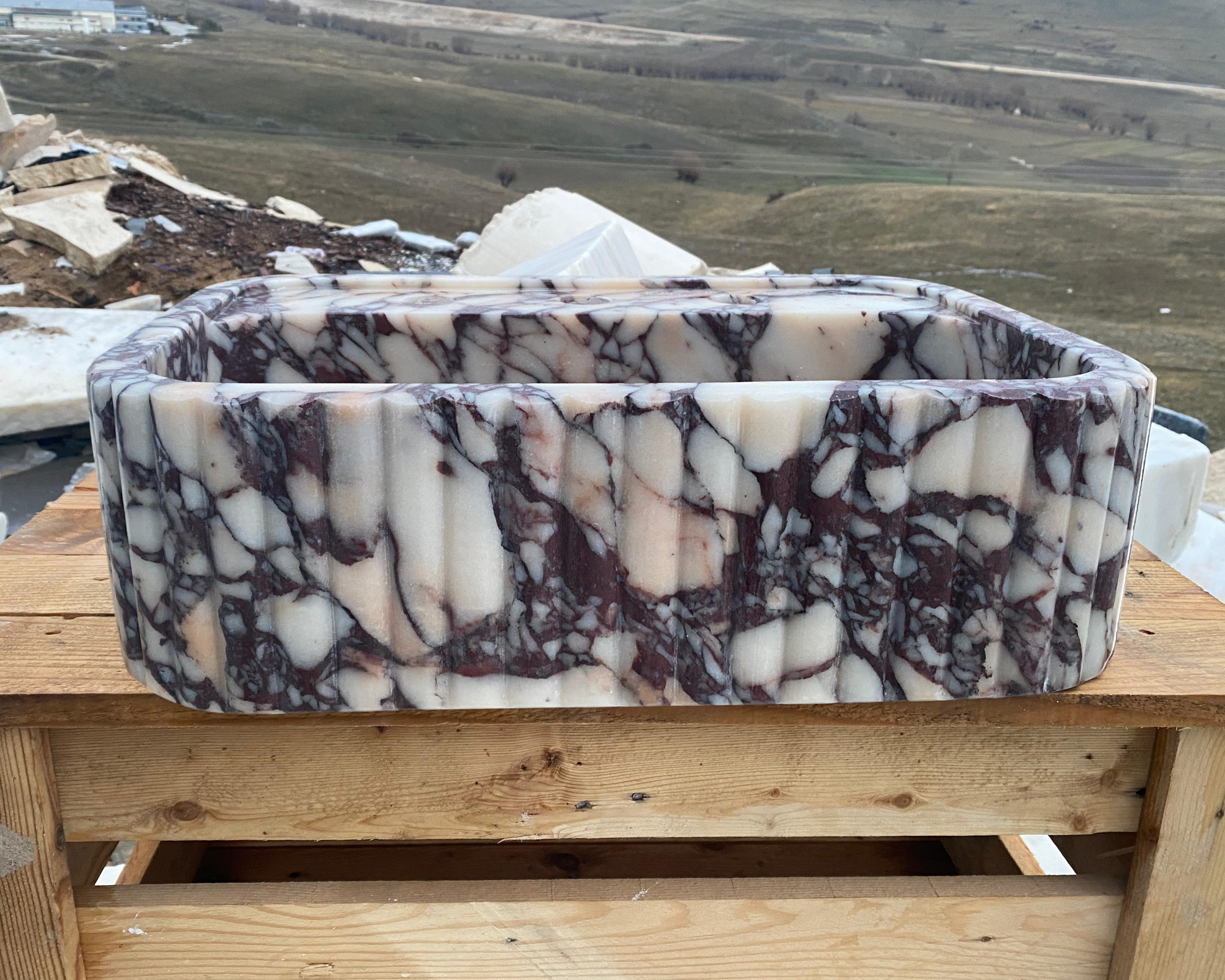 Marble-patterned stone basin on a wooden surface with a landscape in the background