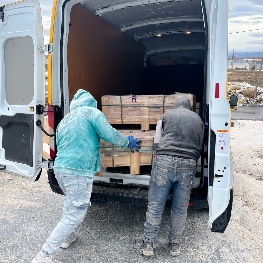 Two workers loading wooden pallets into a van on a cloudy day.
