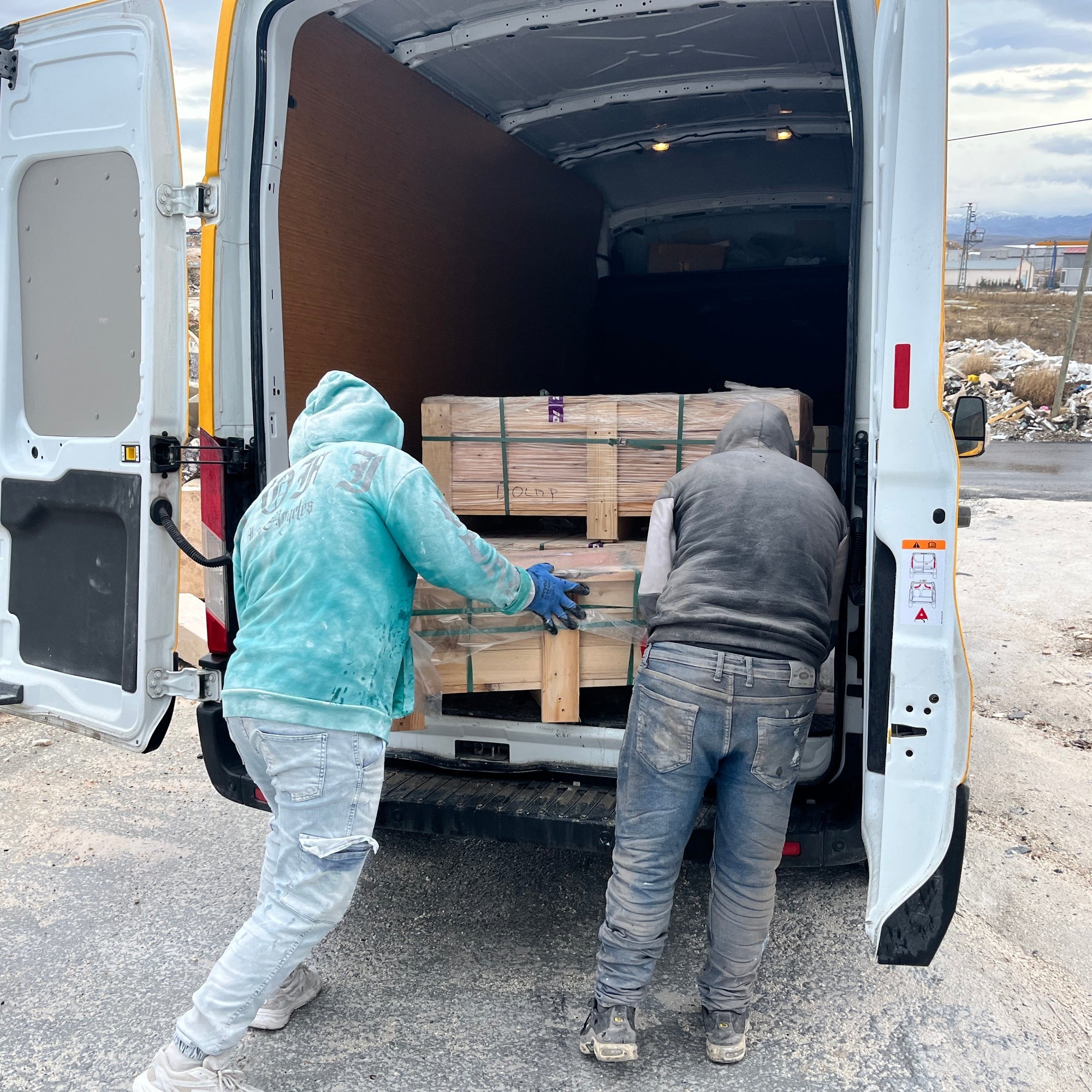 Two workers loading wooden pallets into a van on a cloudy day.